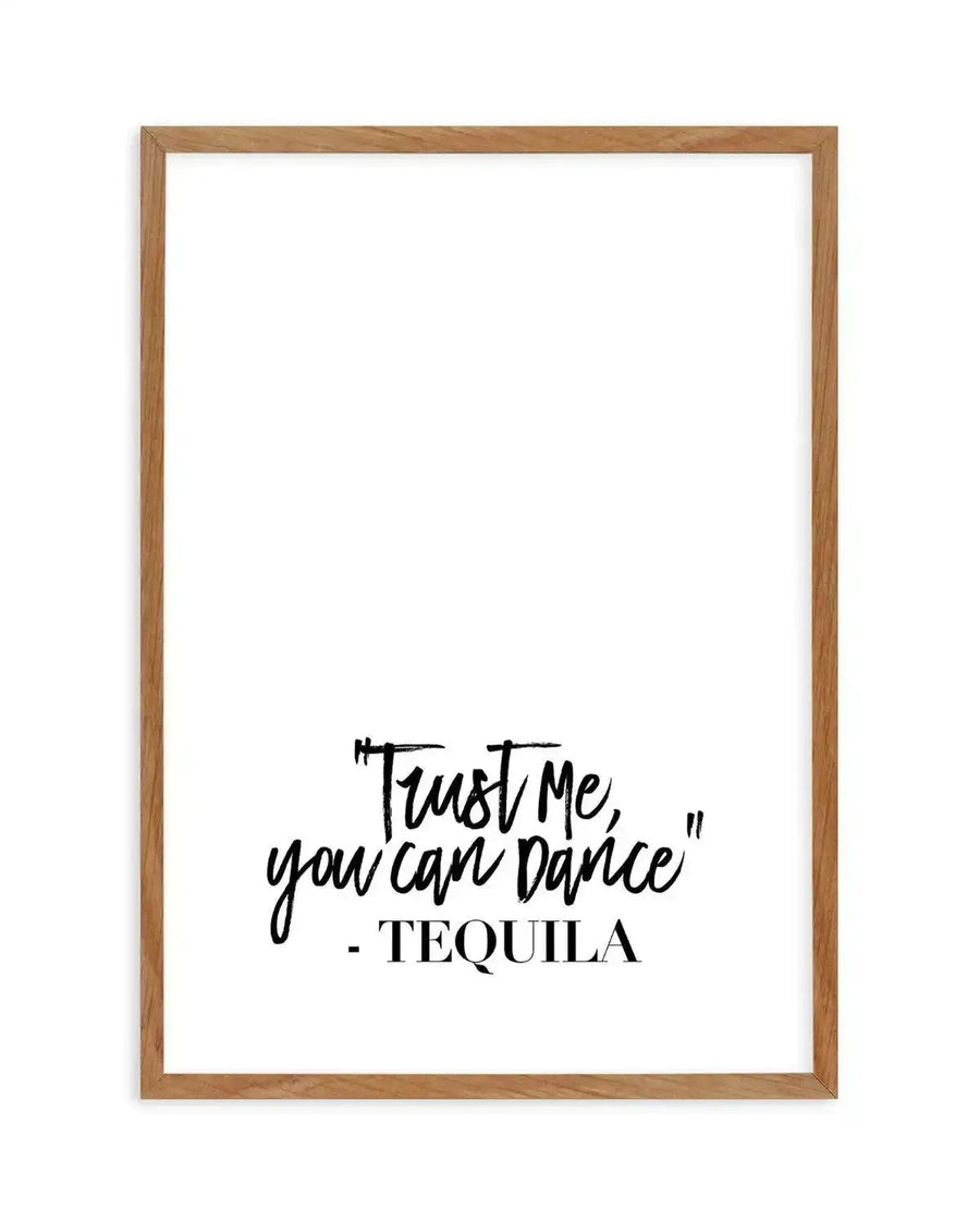 Art print with handwritten-style black text on white background, reading "Trust Me, you can Dance" with "- TEQUILA" below in serif font. The print is displayed in a natural wood frame with visible grain texture.
