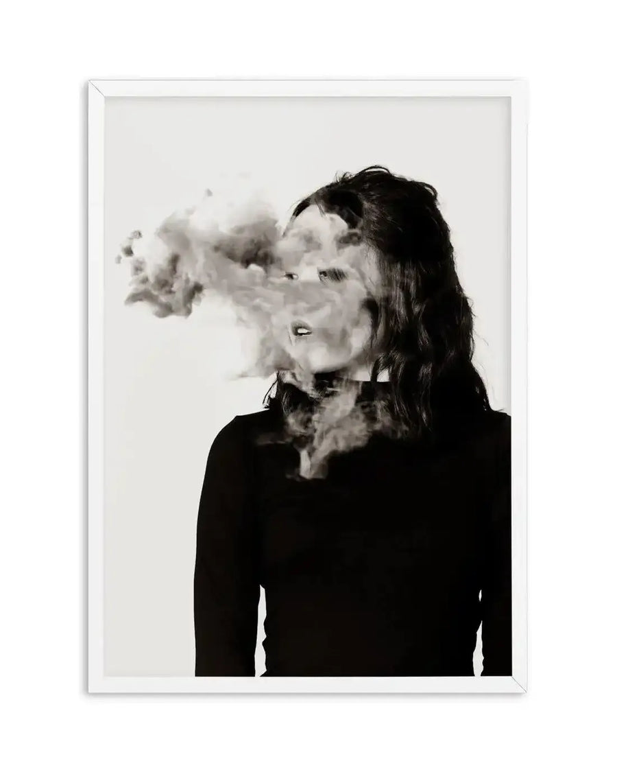 Framed black and white photography art print of a woman with smoke obscuring her face, displayed in a white frame with a white border. The woman has dark, wavy hair and is wearing a dark, long-sleeved top. Smoke billows from her mouth and neck, partially dissolving her facial features into an ethereal, fragmented composition.