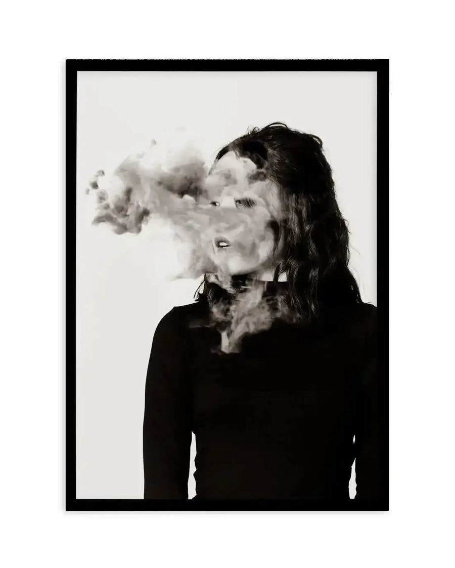 Framed black and white photograph of a woman with long dark hair, facing left, with smoke obscuring her face and rising from her neck, displayed in a black frame with white border. The composition creates a surreal and mysterious mood.