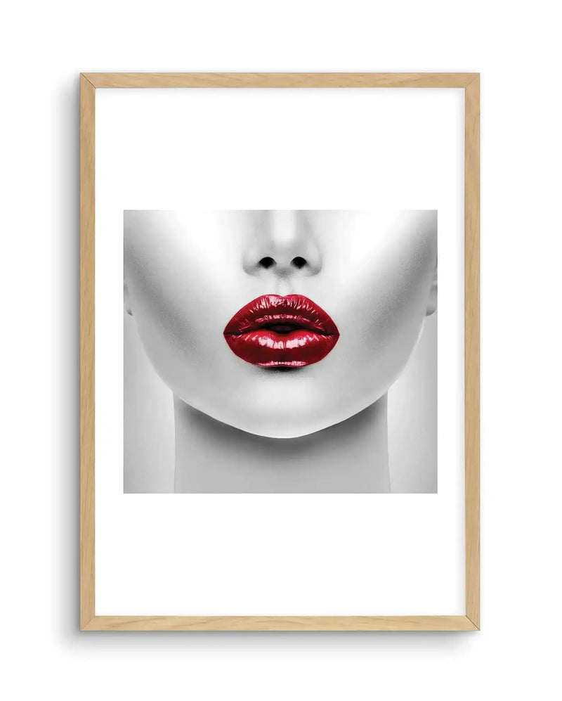 Art print featuring a close-up black and white portrait of the lower half of a face with bold deep red lipstick, displayed in a natural wood frame with white border. The photograph has high contrast grayscale tones with glossy red lips as the focal point. The frame is light natural wood with a simple rectangular design mounted against a white background.