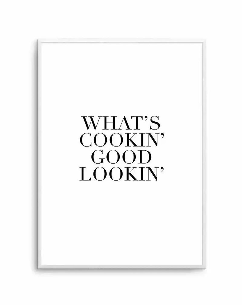 Framed art print featuring the text "WHAT'S COOKIN' GOOD LOOKIN'" displayed in black serif capital letters centered on a white background. The print is mounted in a silver-toned frame with a clean, minimalist design. The typography uses an elegant, classic serif font with even spacing between the words arranged in four lines.