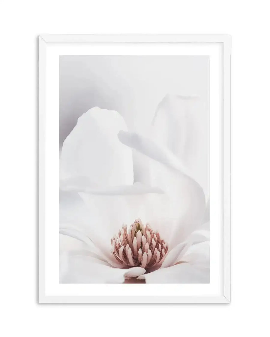 Framed photography art print of a close-up white magnolia flower with a white frame and white border. The composition focuses on the delicate, soft white petals and the prominent pink and green pistil and stamens at the center, creating a serene and elegant mood.