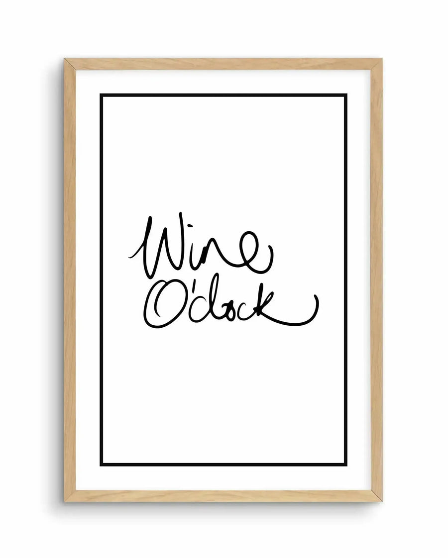 Framed art print with natural wood frame displaying handwritten-style text reading "Wine O'Clock" in black ink on white background with white border. The text is written in a flowing, cursive script with decorative flourishes on a vertical rectangular print.