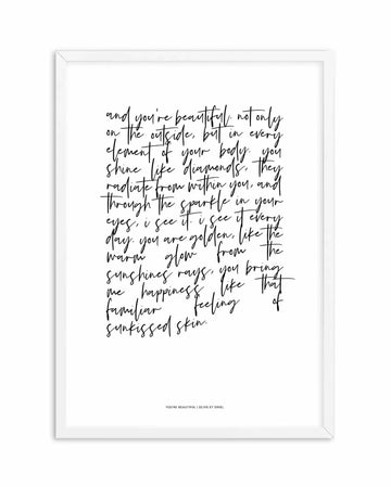 A framed art print with handwritten script on white background. The text is a poem about inner and outer beauty, written in black cursive handwriting that flows across the page. The frame is white wood with a simple border. At the bottom of the print, small black text reads "YOU'RE BEAUTIFUL | OLIVE ET ORIEL". The handwriting style is loose and organic, giving the piece an intimate, personal quality. The overall composition is centered on the white matte surface.