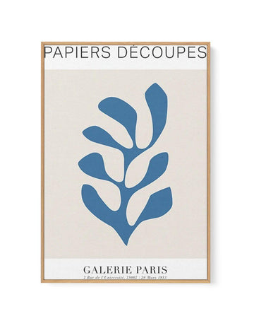 Framed canvas art print with natural wood frame displaying an abstract botanical illustration. The design features a stylized blue plant or seaweed form with organic, teardrop-shaped leaves branching upward from a central stem in muted slate blue against a cream background. French text reads "Papiers Decoupes" at top and "Galerie Paris" with exhibition details at bottom. The composition has a minimalist, mid-century modern aesthetic with clean lines and generous white space.